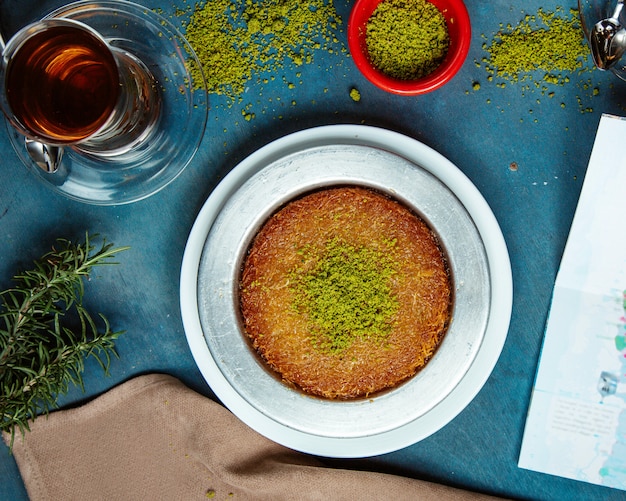 Vue de dessus du dessert kunefe garni de pistaches servi avec du thé noir