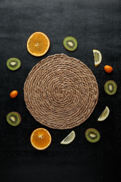 Vue de dessus du dessous de plat pour plats chauds avec des tranches d'orange kiwi et de citron autour sur fond noir