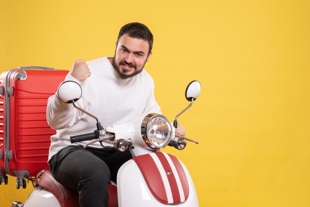 Vue de dessus du fier jeune homme assis sur une moto avec une valise dessus et profitant de son succès sur fond jaune isolé