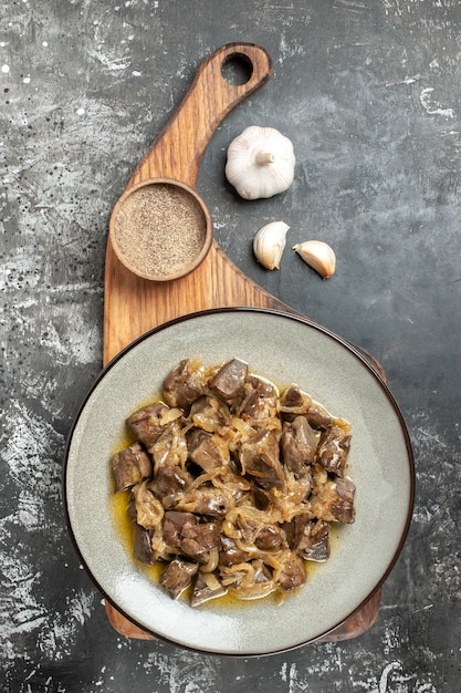 Vue de dessus du foie et de l'oignon cuits sur une assiette de poivre noir sur une planche à découper de l'ail sur une table grise