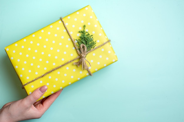 Vue De Dessus Du Fond De Noël Avec Une Main Tenant Une Boîte-cadeau Jaune Sur Fond Vert Pastel Photo gratuit