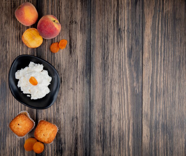 Vue de dessus du fromage cottage dans un bol noir avec des muffins pêches fraîches et abricots secs sur une table en bois rustique avec espace copie