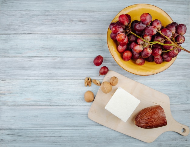 Vue de dessus du fromage fumé et du fromage feta sur une planche à découper en bois avec des noix et des raisins doux dans une assiette sur une table rustique avec espace copie