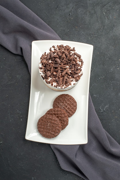 Vue de dessus du gâteau au chocolat et des biscuits sur une assiette rectangulaire blanche châle violet sur fond sombre isolé