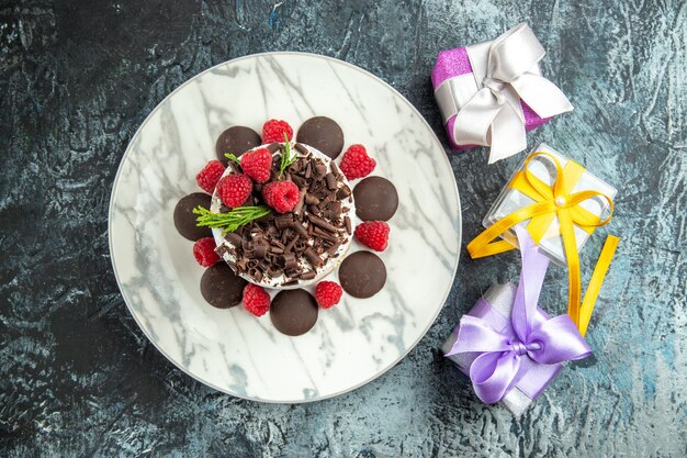 Vue de dessus du gâteau au fromage avec du chocolat sur des cadeaux de Noël plaque ovale sur surface grise