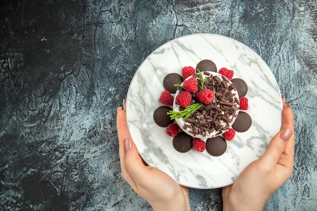 Vue de dessus du gâteau au fromage avec du chocolat sur une plaque ovale dans les mains de la femme sur la surface grise place libre