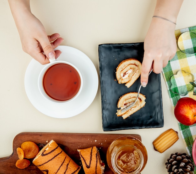 Vue de dessus du gâteau au rouleau portant sur un plateau noir et tenant une tasse de thé et un bocal en verre avec des biscuits à la confiture de pêches nectarines mûres fraîches et emporte-pièces sur blanc