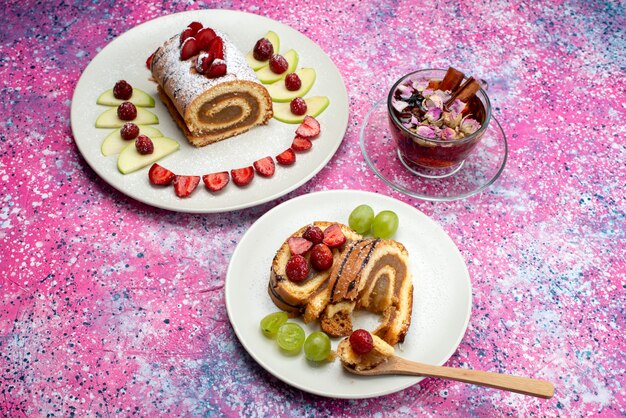 Vue de dessus du gâteau aux fruits à l'intérieur de la plaque blanche avec du thé sur le fond coloré gâteau biscuit couleur douce