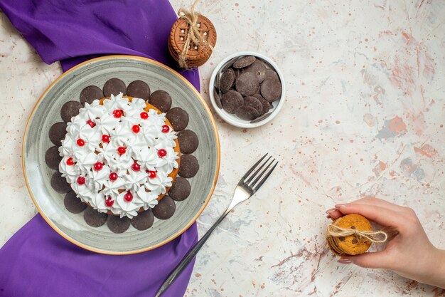 Vue de dessus du gâteau avec de la crème pâtissière sur une assiette ovale des biscuits châle violets attachés avec des biscuits de fourche à corde dans une main féminine