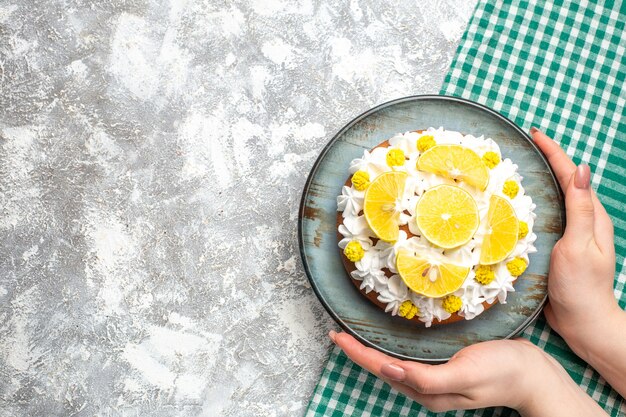 Vue de dessus du gâteau avec de la crème pâtissière blanche et des tranches de citron sur une assiette ronde dans une main féminine