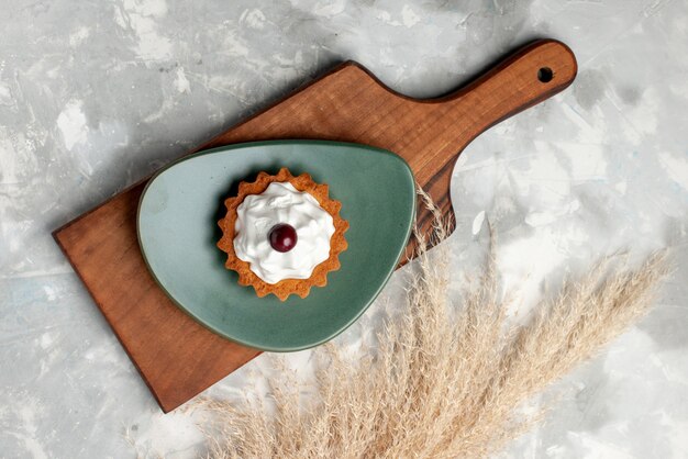 Photo gratuite vue de dessus du gâteau à la crème avec plaque à l'intérieur de la cerise sur le bureau gris clair, gâteau biscuit sucre sucré