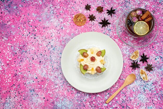 Vue de dessus du gâteau avec de la crème et des tranches de fruits avec du thé sur le fond coloré gâteau biscuit couleur sucre sucré