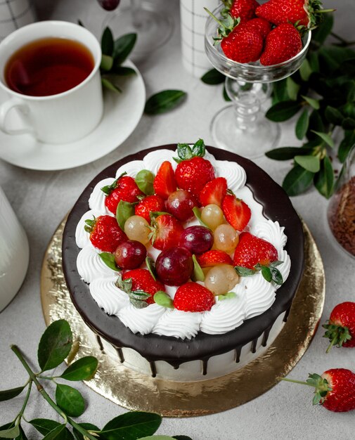 Vue de dessus du gâteau dégoulinant de chocolat garni de fraises et de raisins