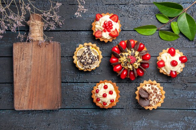 Vue de dessus du gâteau avec des feuilles de tartelettes aux framboises et au chocolat aux fruits de cornel et une planche à découper sur une surface sombre