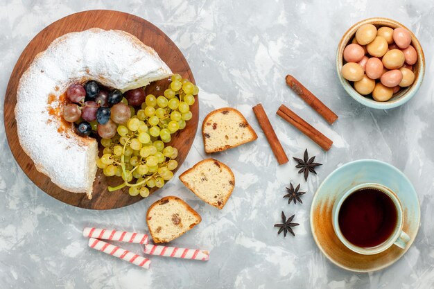 Vue de dessus du gâteau en poudre délicieux gâteau cuit au four avec des raisins frais et une tasse de thé sur un bureau blanc