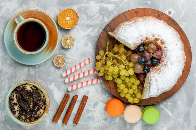 Vue de dessus du gâteau en poudre avec des raisins frais, de la cannelle et des macarons sur la surface blanche