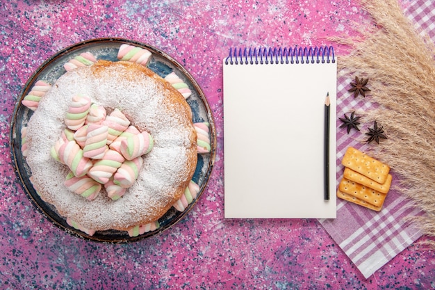 Vue de dessus du gâteau en poudre de sucre avec des craquelins et bloc-notes sur la surface rose