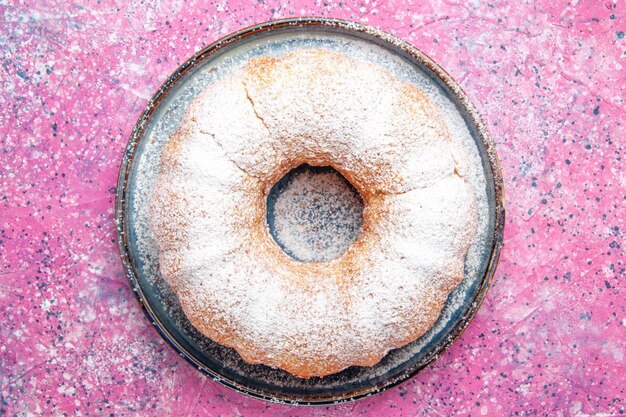 Vue de dessus du gâteau en poudre de sucre rond formé sur une surface rose