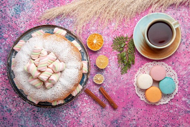 Vue de dessus du gâteau en poudre de sucre avec tasse de thé et macarons sur surface rose
