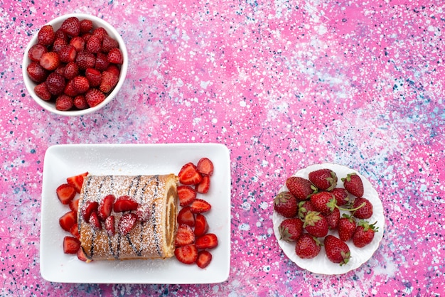 Vue de dessus du gâteau roulé avec des fraises rouges à l'intérieur des assiettes sur le fond coloré gâteau biscuit couleur douce