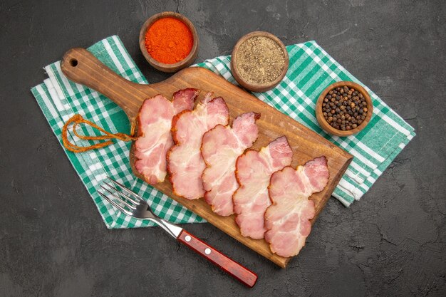 Vue de dessus du jambon frais tranché avec des assaisonnements sur un bureau gris foncé