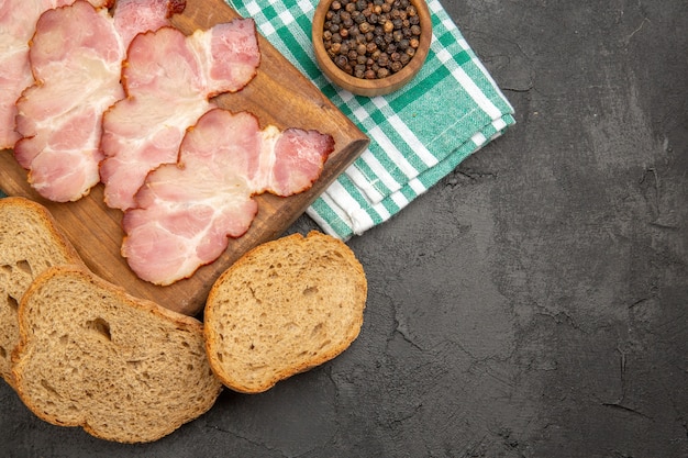 Photo gratuite vue de dessus du jambon frais en tranches avec du pain d'assaisonnement et des grenades sur fond sombre