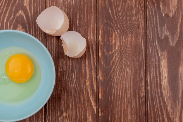 Vue de dessus du jaune d'oeuf et blanc sur un bol blanc avec des coquilles d'oeuf fêlé sur un fond en bois avec copie espace