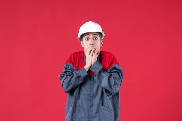 Vue de dessus du jeune constructeur effrayé en uniforme avec un casque sur un mur rouge isolé