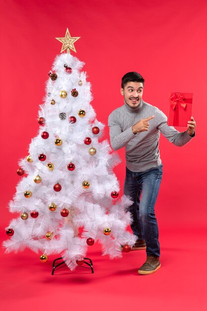 Vue de dessus du jeune homme debout près de l'arbre du nouvel an blanc décoré et tenant son cadeau