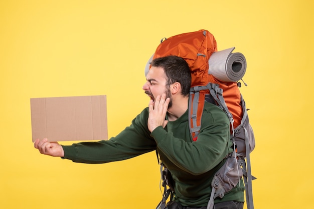 Vue de dessus du jeune homme de voyage émotionnel nerveux avec sac à dos tenant une feuille sans écrire sur le jaune