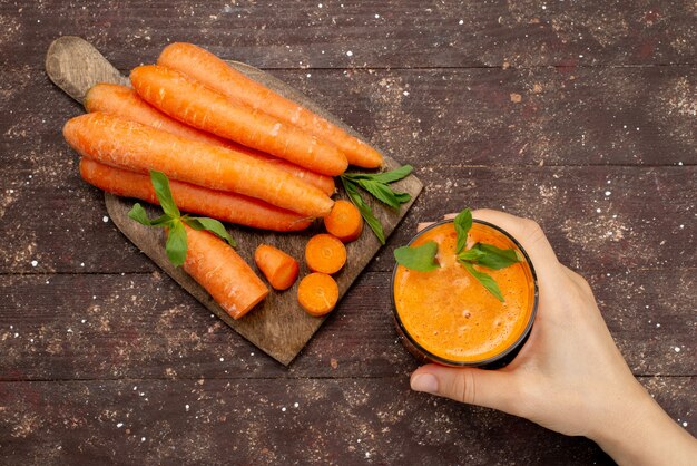 Vue de dessus du jus de carotte frais à l'intérieur d'un long verre avec des feuilles et avec des carottes fraîches sur brun