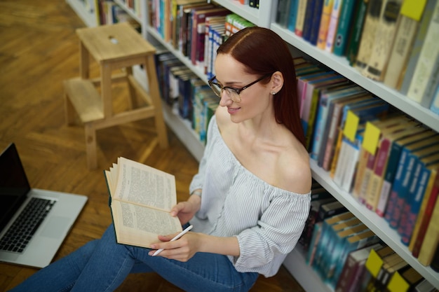 Vue de dessus du livre de lecture de femme assise sur le sol