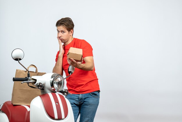 Vue de dessus du livreur perplexe en uniforme rouge debout près de scooter donnant l'ordre sur fond blanc