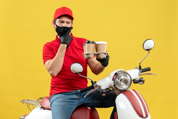 Vue de dessus du livreur portant des gants uniformes et chapeau en masque médical assis sur un scooter montrant les commandes se sentant choqué