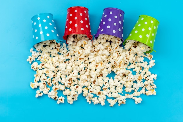 Une vue de dessus du maïs soufflé frais à l'intérieur de paniers colorés répartis sur le bleu, snack de maïs cinéma