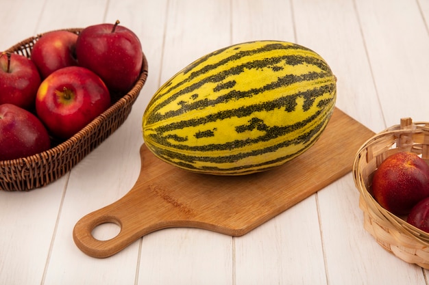 Vue de dessus du melon cantaloup biologique sur une planche de cuisine en bois avec des pommes sur un seau avec des pêches sur un fond en bois blanc