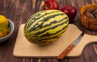 Photo gratuite vue de dessus du melon cantaloup frais sur une planche de cuisine en bois avec couteau avec pommes isolé sur un mur en bois