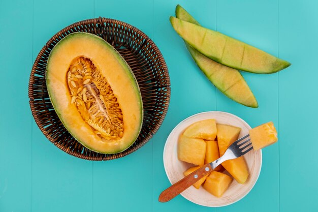 Vue de dessus du melon cantaloup sucré mûr sur une planche de cuisine en bois avec des tranches sur un bol avec une fourchette sur une surface bleue