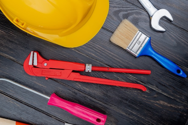 Vue de dessus du modèle de l'ensemble d'outils de construction comme clé à tube tournevis casque de sécurité pinceau et clé à fourche sur fond de bois