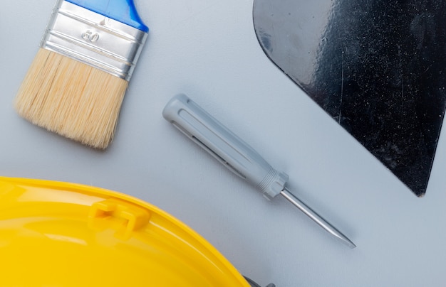 Photo gratuite vue de dessus du modèle de l'ensemble d'outils de construction comme tournevis casque de sécurité mastic couteau pinceau sur fond gris