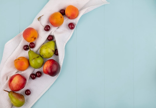 Photo gratuite vue de dessus du modèle de fruits comme poire abricot pêche cerise sur tissu blanc et fond bleu avec espace copie