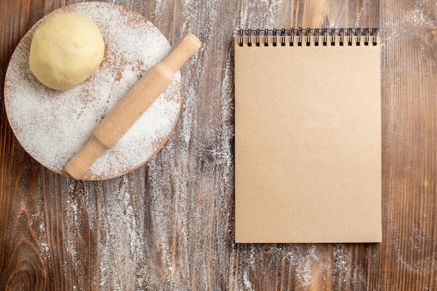 Vue de dessus du morceau de pâte crue avec de la farine sur un bureau en bois