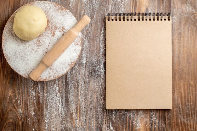 Vue de dessus du morceau de pâte crue avec de la farine sur un bureau en bois