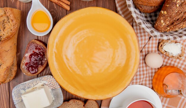 Vue de dessus du pain comme des tranches de pain de seigle de baguettes aux graines croustillantes avec du beurre de confiture d'oeuf thé cannelle autour de la plaque sur fond de bois