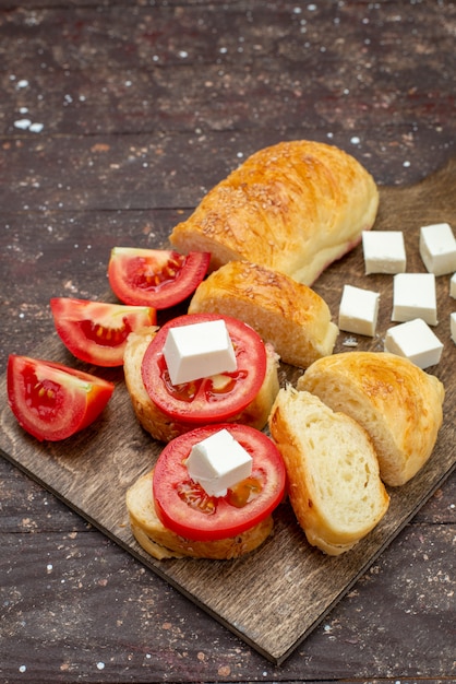 Vue de dessus du pain savoureux frais long pain formé pâte coupée avec du fromage et des tomates sur le bureau en bois brun pain de pâte à pâtisserie repas