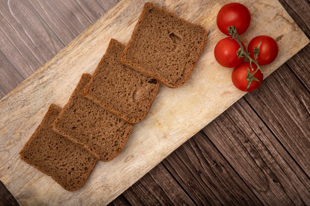 Vue de dessus du pain de seigle en tranches et des tomates sur une planche à découper sur fond de bois