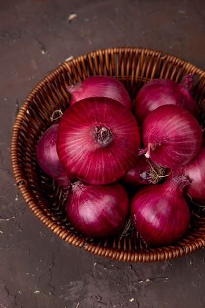 Vue de dessus du panier d'oignons rouges sur fond marron