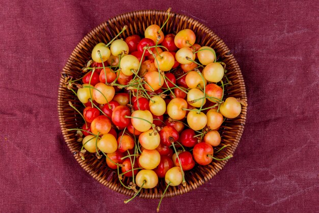 Photo gratuite vue de dessus du panier plein de cerises jaunes et rouges sur la surface en tissu bordo