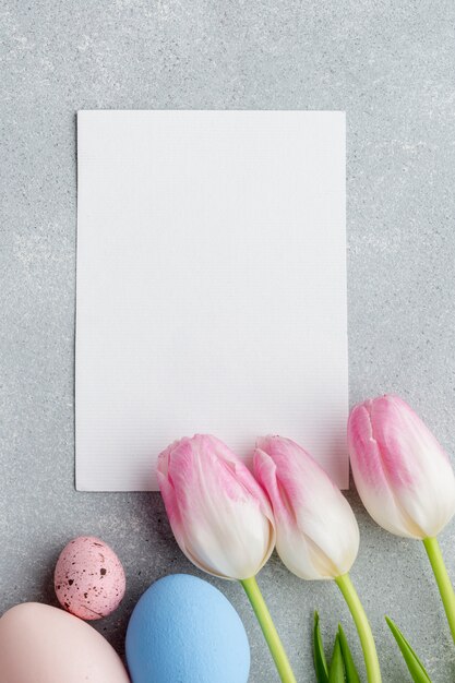 Vue de dessus du papier vierge avec des tulipes et des oeufs de Pâques colorés