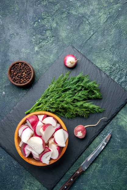 Vue de dessus du paquet d'aneth frais et couteau de radis haché entier sur une planche à découper noire couteau à poivre sur fond de couleurs de mélange noir vert avec espace libre